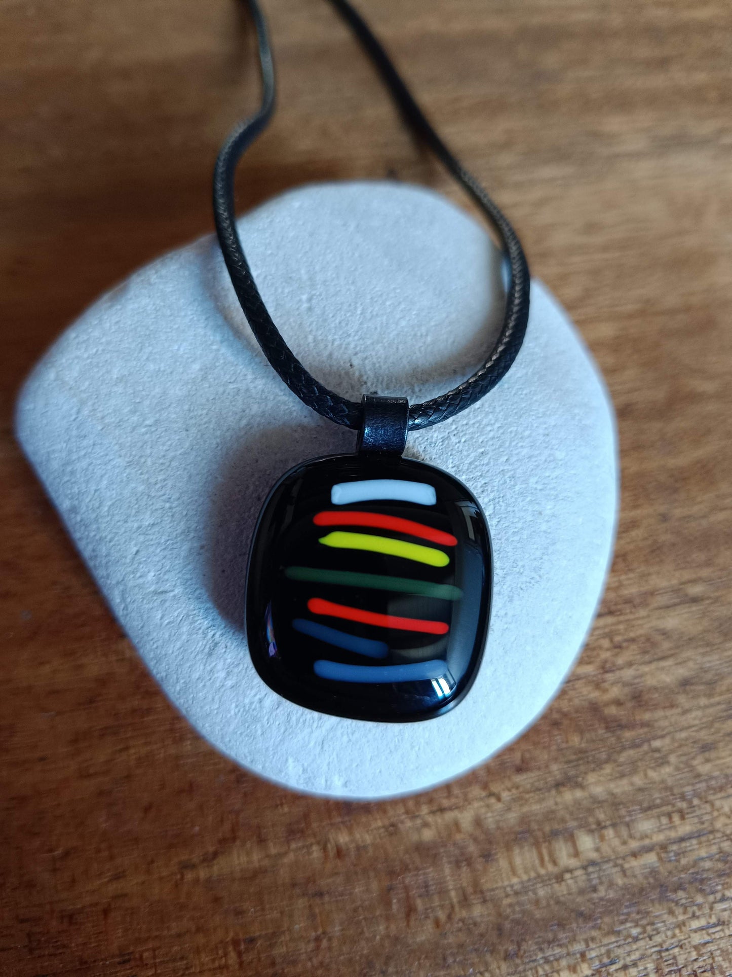 colourful fused glass pendant laying on a stone