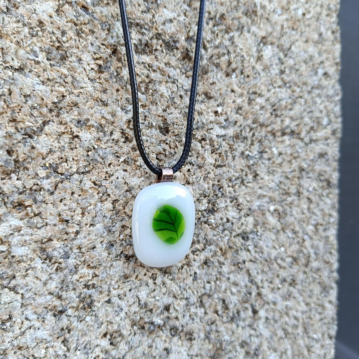 A white glass pendant with a green leaf design on a black cord necklace.