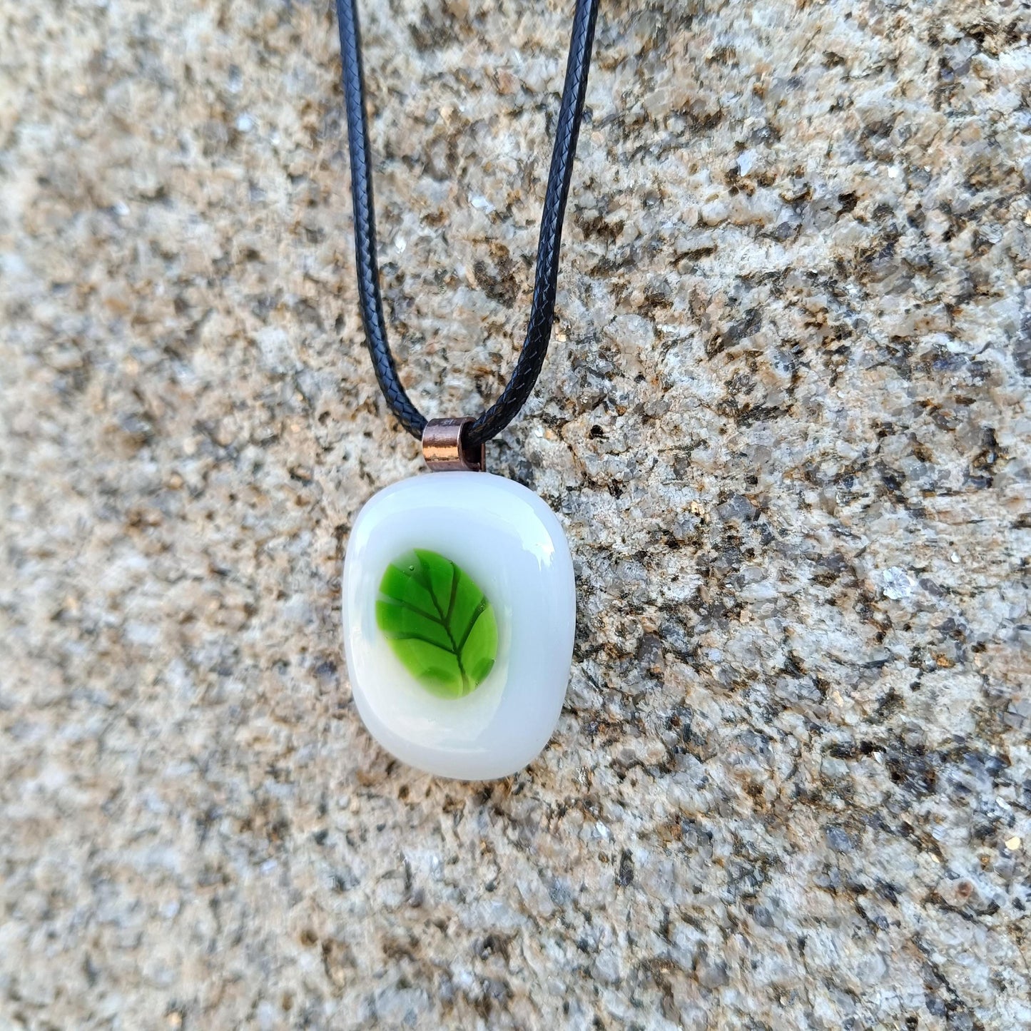 A white glass pendant with a green leaf design on a black cord necklace.