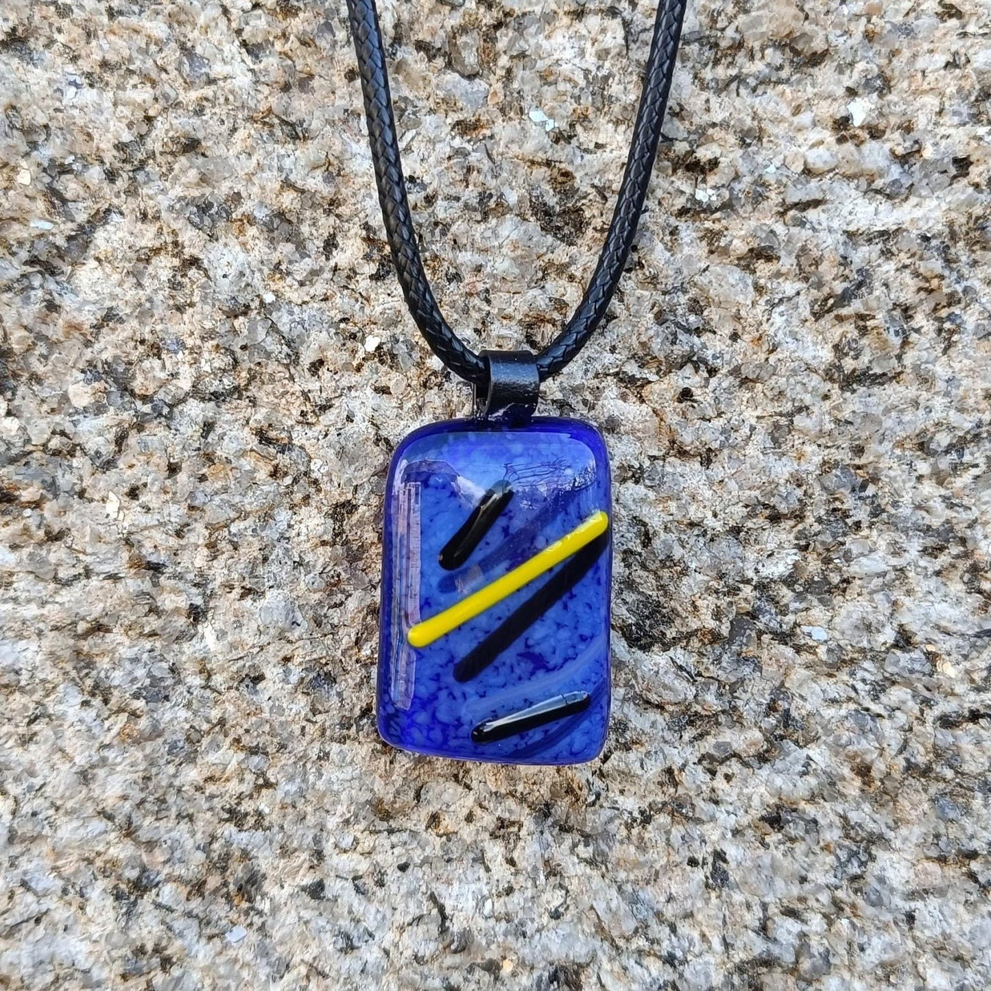 blue black and yellow fused glass necklace handmade with cord hanging on a wall