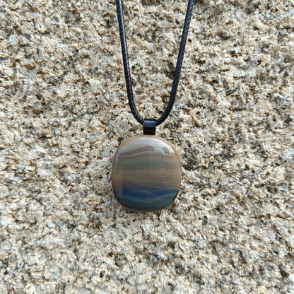 glass pendant on a cord hanging against a granite wall