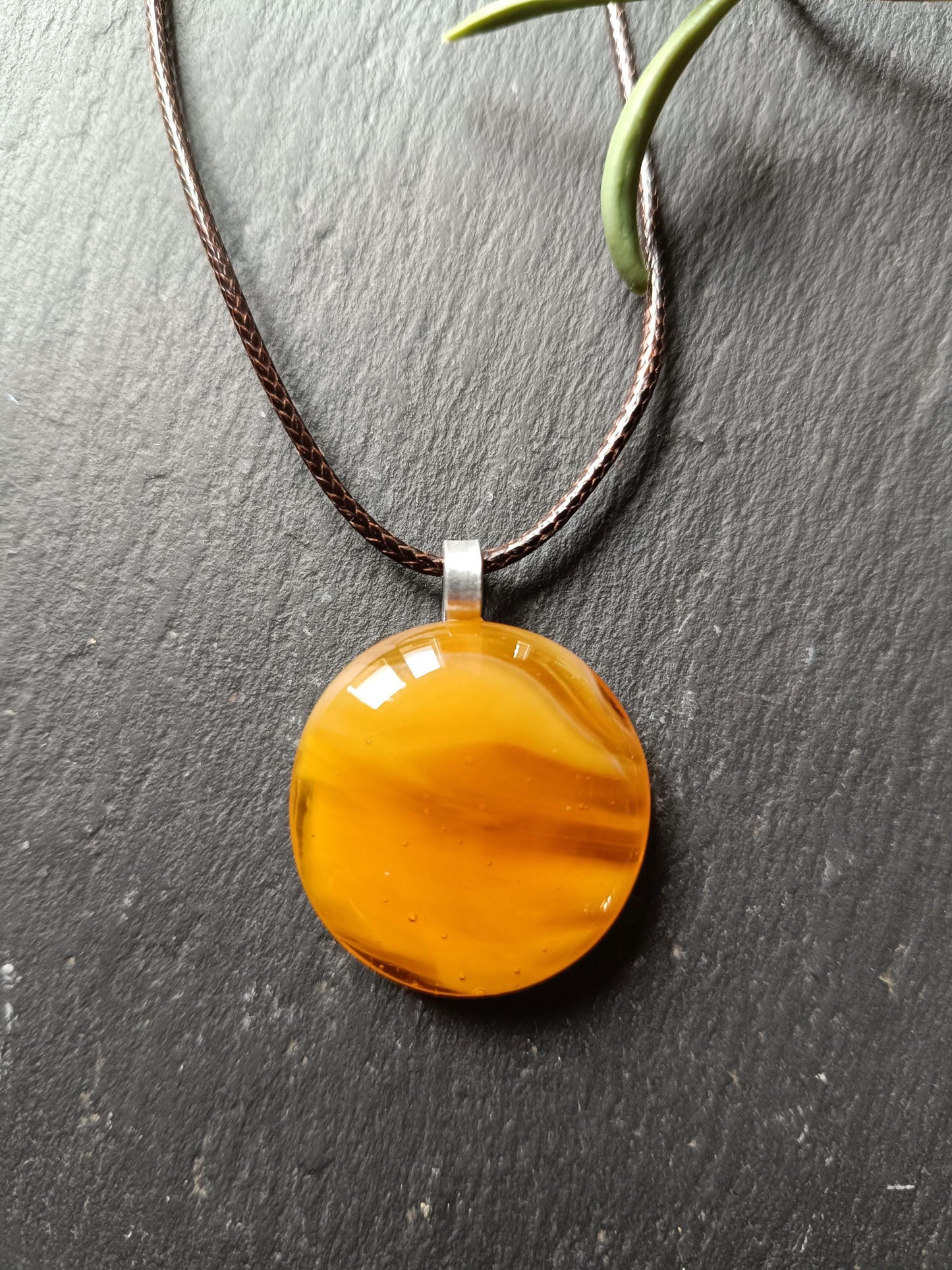 light warm coloured transparent glass pendant streaky on a cord necklace presented on a slate