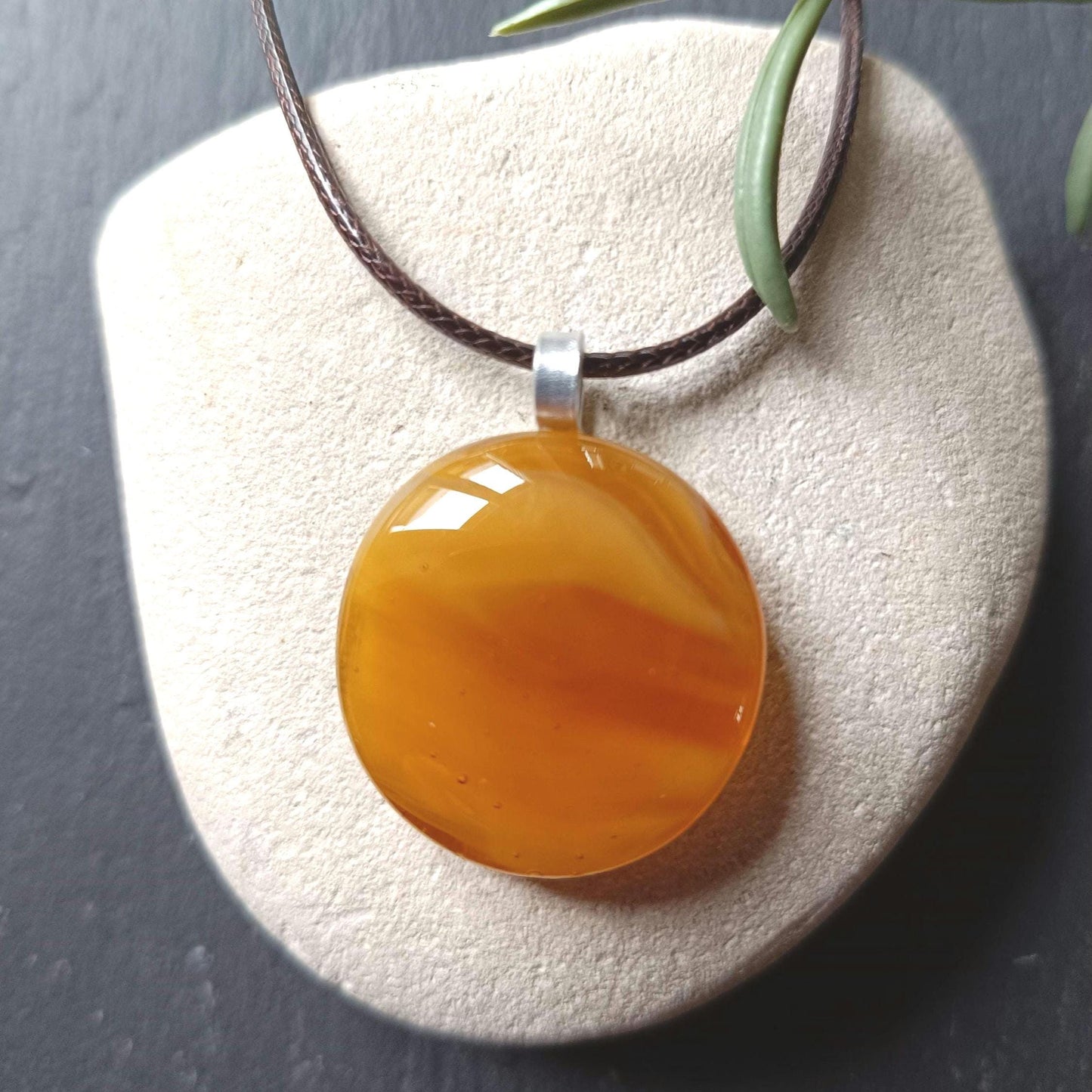 light warm coloured transparent glass pendant streaky on a cord necklace presented on a white stone