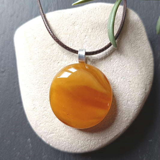 light warm coloured transparent glass pendant streaky on a cord necklace presented on a white stone
