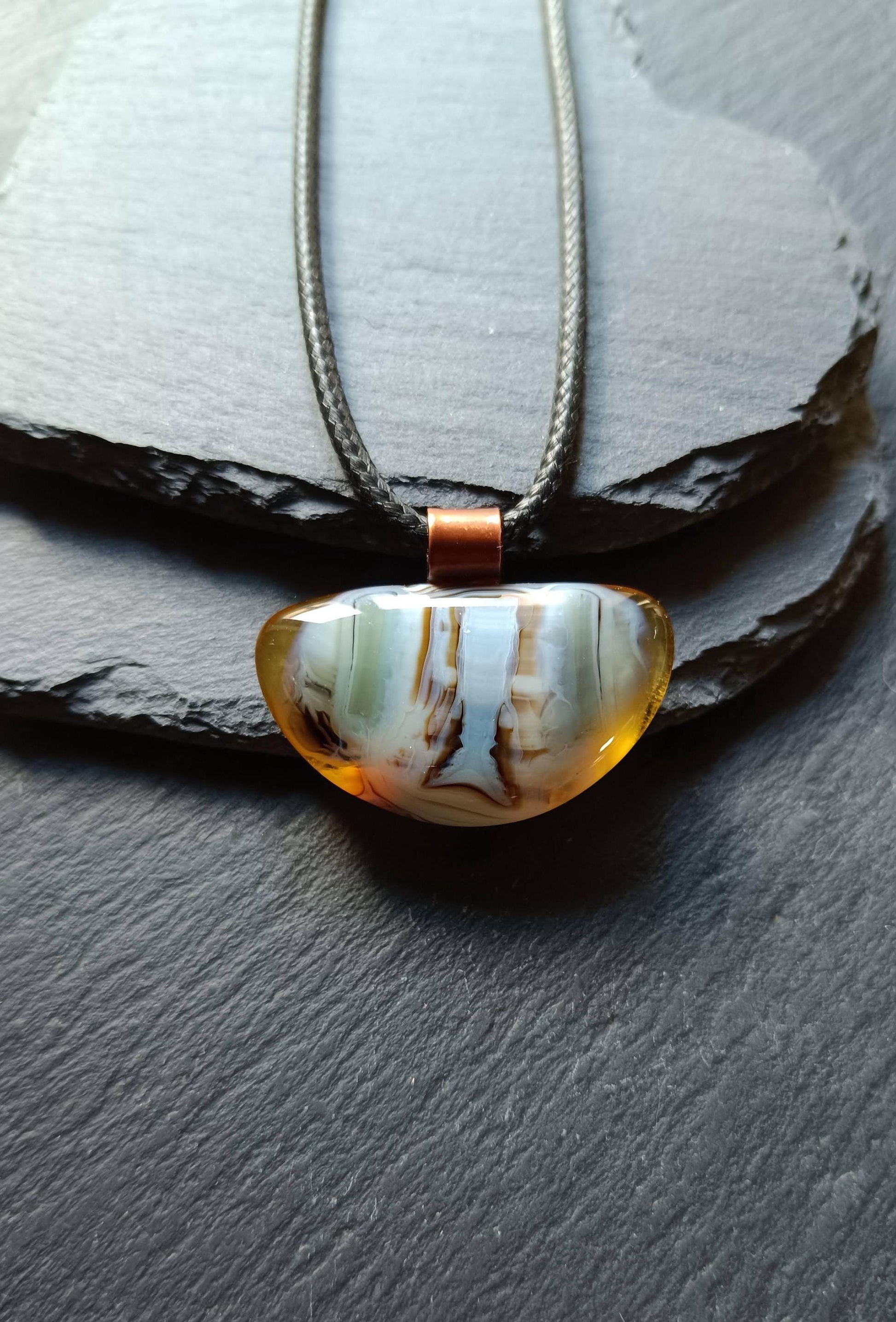 Fused glass pendant on a grunge black cord necklace with copper bail; orange bottom with blue-green swirls and brown lines.