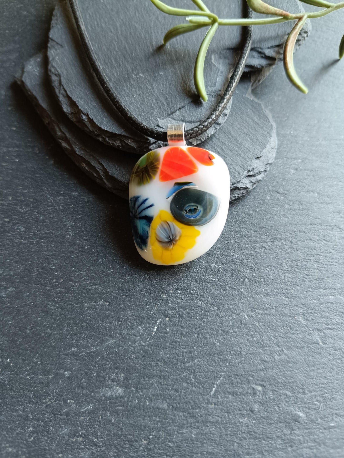 Oval fused glass pendant on black cord, handmade jewellery with bright floral patterns—bold statement piece.