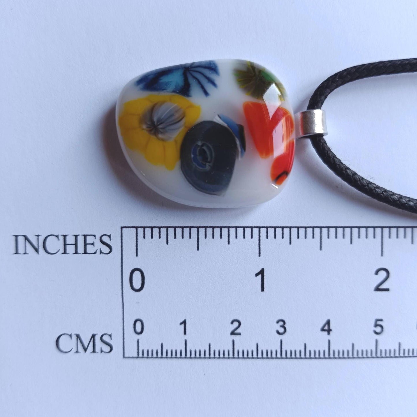 Oval fused glass pendant on black cord, handmade jewellery with bright floral patterns—bold statement piece.