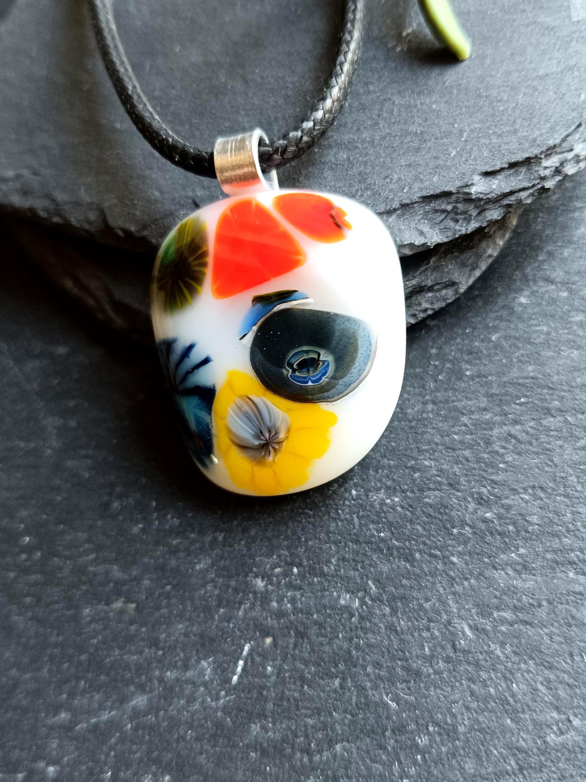 Oval fused glass pendant on black cord, handmade jewellery with bright floral patterns—bold statement piece.