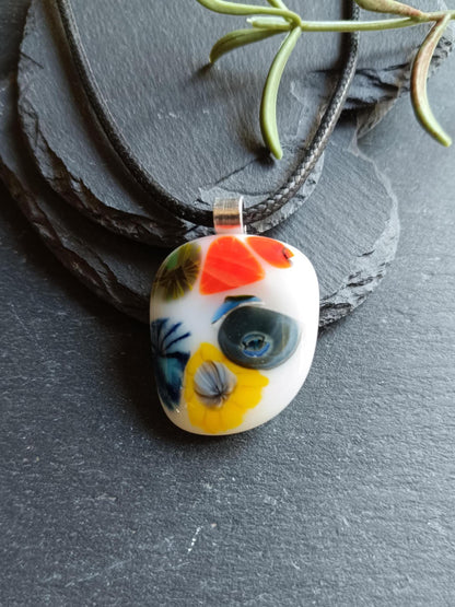 Oval fused glass pendant on black cord, handmade jewellery with bright floral patterns—bold statement piece.
