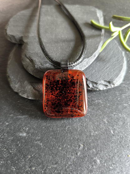 Red transparent fused glass pendant on a dark cord necklace; handmade necklace with black speckles.