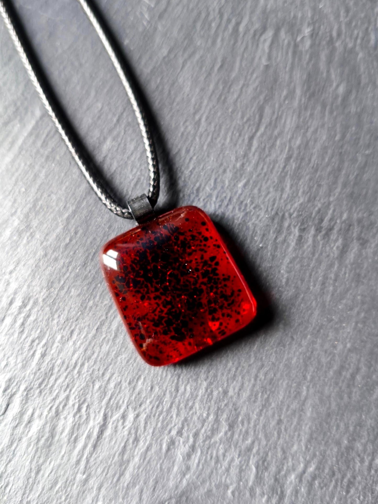 Red transparent fused glass pendant on a dark cord necklace; handmade necklace with black speckles.