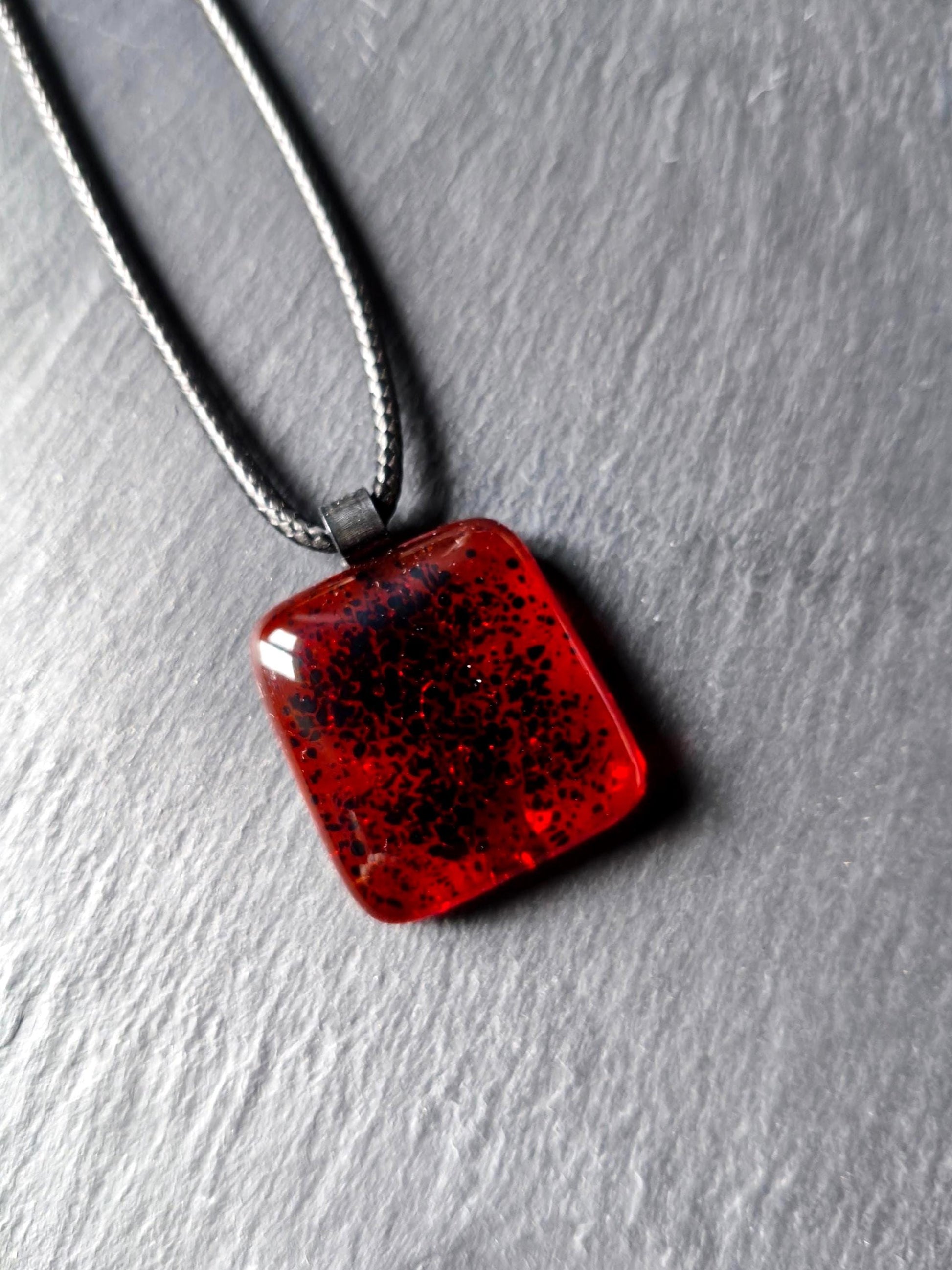 Red transparent fused glass pendant on a dark cord necklace; handmade necklace with black speckles.