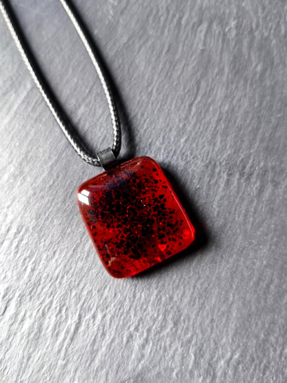 Red transparent fused glass pendant on a dark cord necklace; handmade necklace with black speckles.