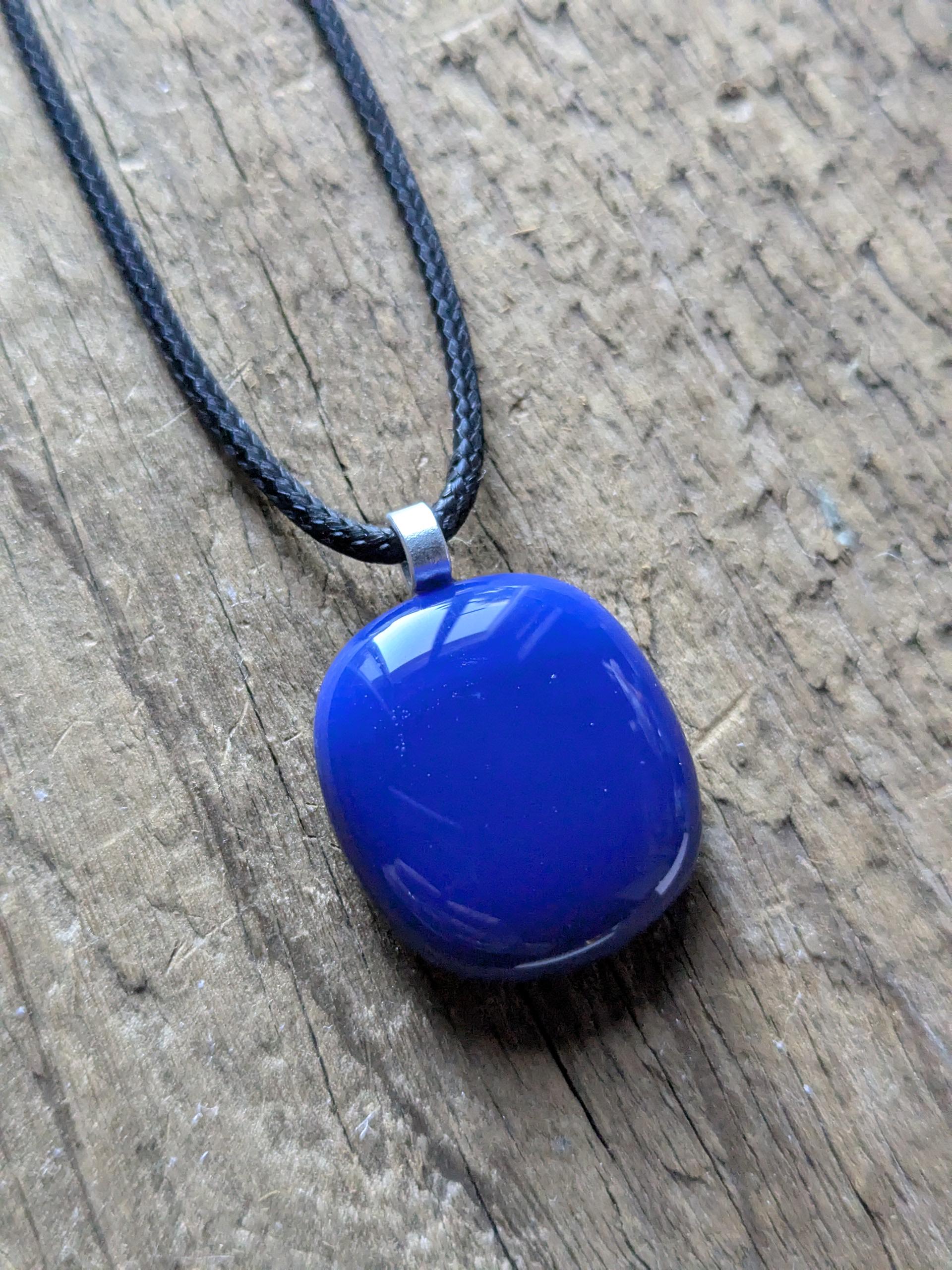 Blue fused glass pendant on a black cord necklace; smooth cobalt-blue oval pendant, handmade artisan jewelry.