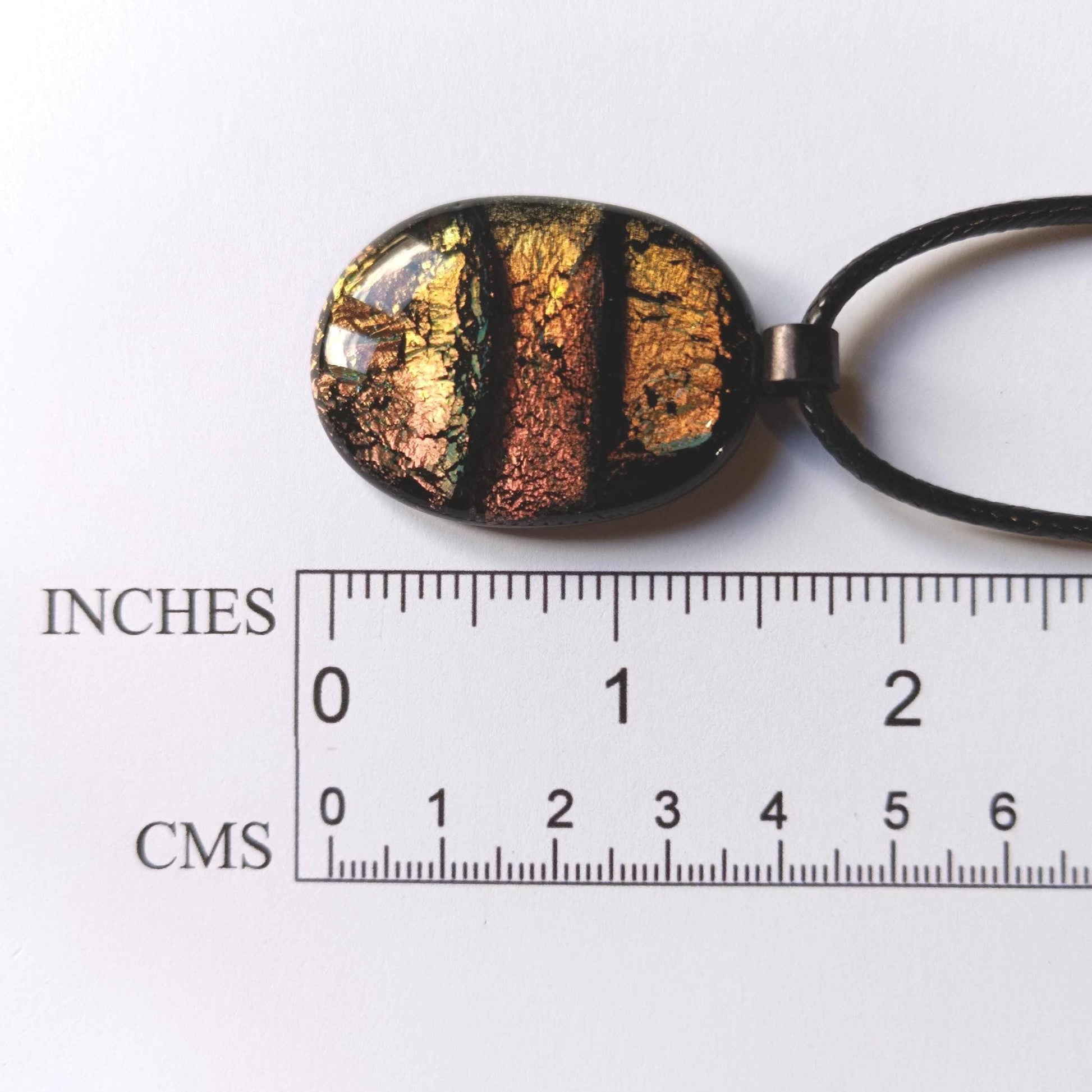 Oval handmade dichroic fused glass pendant in warm amber-copper tones on a black cord, layered design with metallic edges.