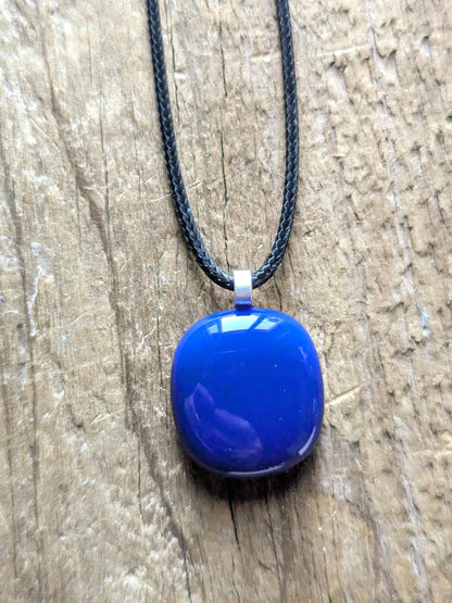 Blue fused glass pendant on a black cord necklace; smooth cobalt-blue oval pendant, handmade artisan jewelry.