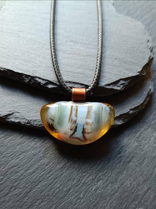 Fused glass pendant on a grunge black cord necklace with copper bail; orange bottom with blue-green swirls and brown lines.