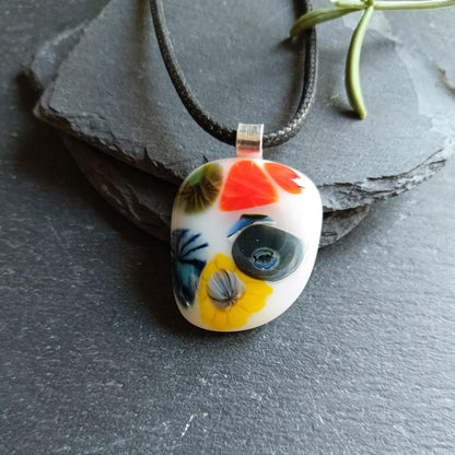 Oval fused glass pendant on black cord, handmade jewellery with bright floral patterns—bold statement piece.