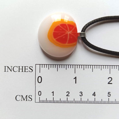 Fused glass orange pendant necklace on black cord; white round disc with bright orange slice, handmade one-of-a-kind jewelry.
