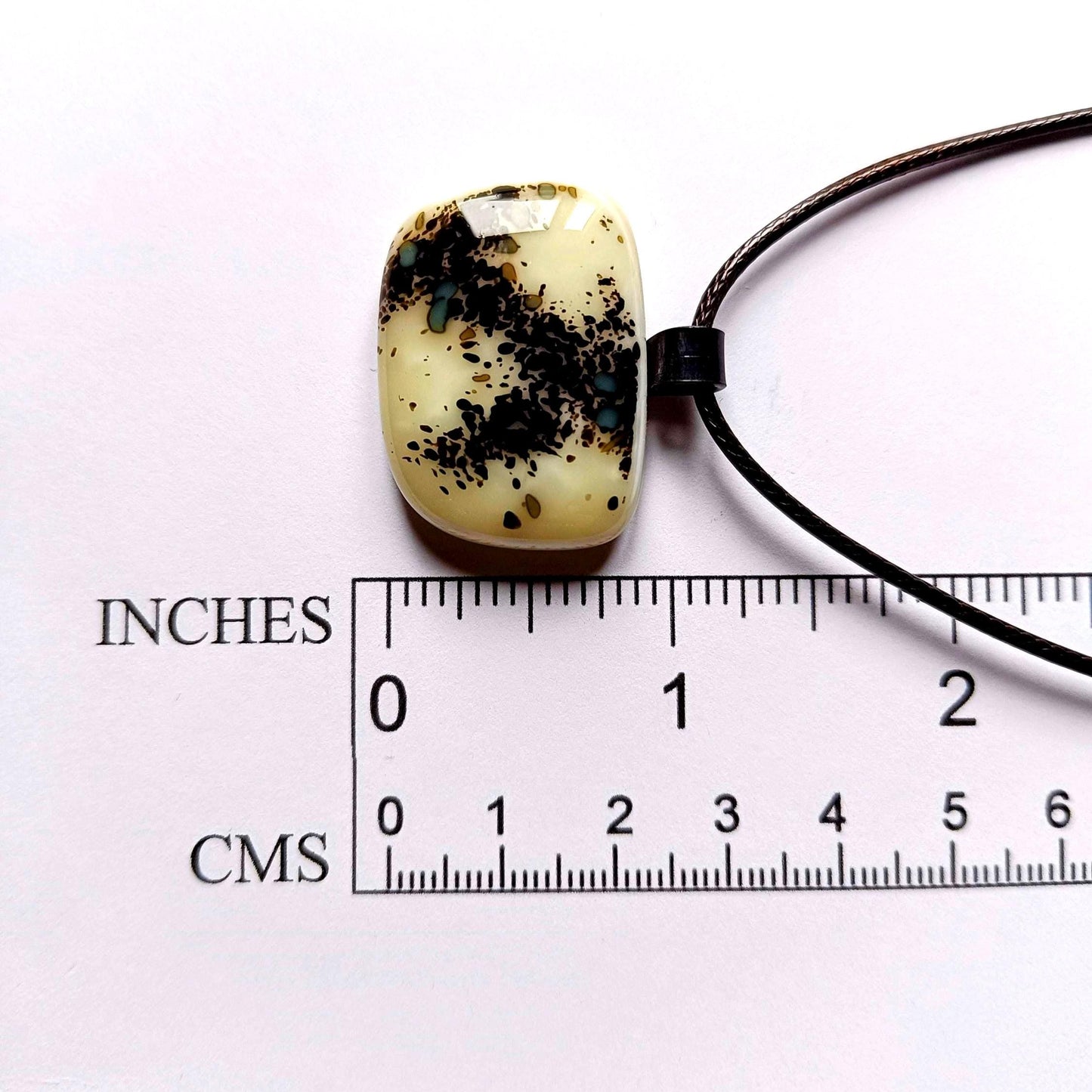 One-of-a-kind fused glass pendant on dark cord; cream vanilla with black splatters and teal specks, handmade boho Gothic.