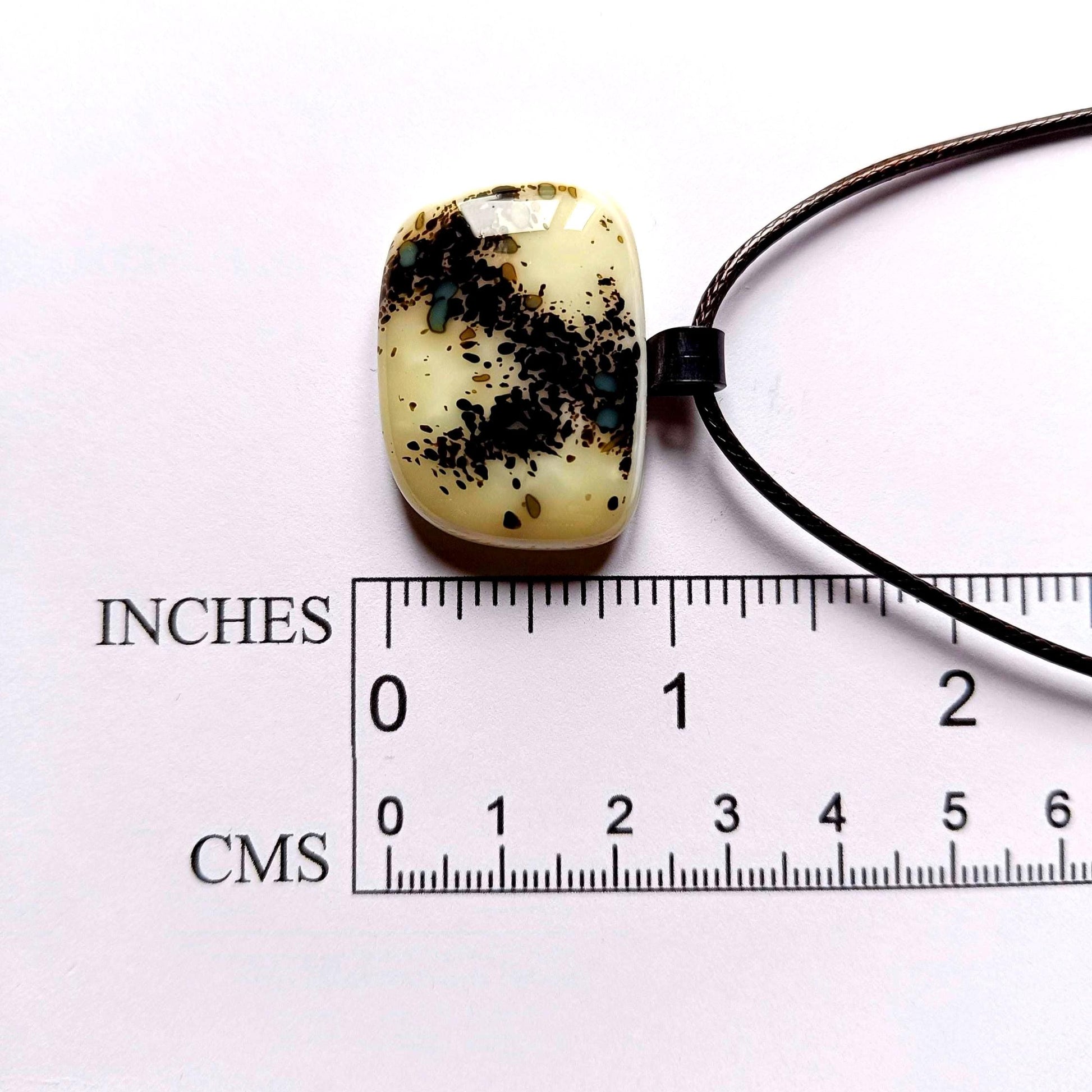 One-of-a-kind fused glass pendant on dark cord; cream vanilla with black splatters and teal specks, handmade boho Gothic.