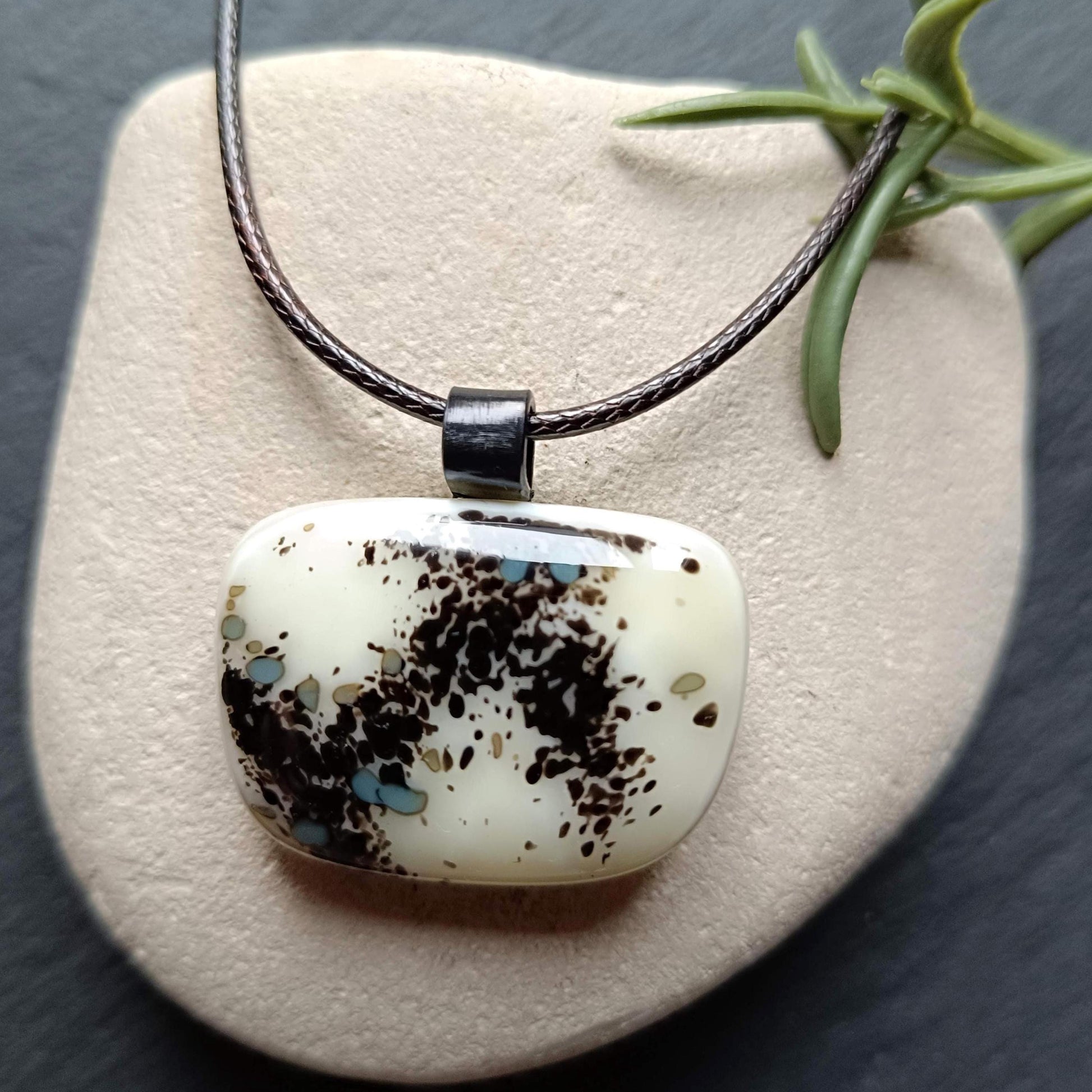 One-of-a-kind fused glass pendant on dark cord; cream vanilla with black splatters and teal specks, handmade boho Gothic.