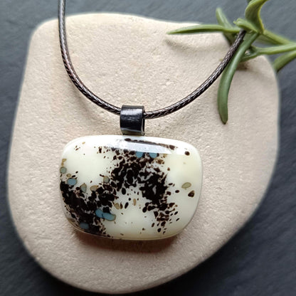 One-of-a-kind fused glass pendant on dark cord; cream vanilla with black splatters and teal specks, handmade boho Gothic.
