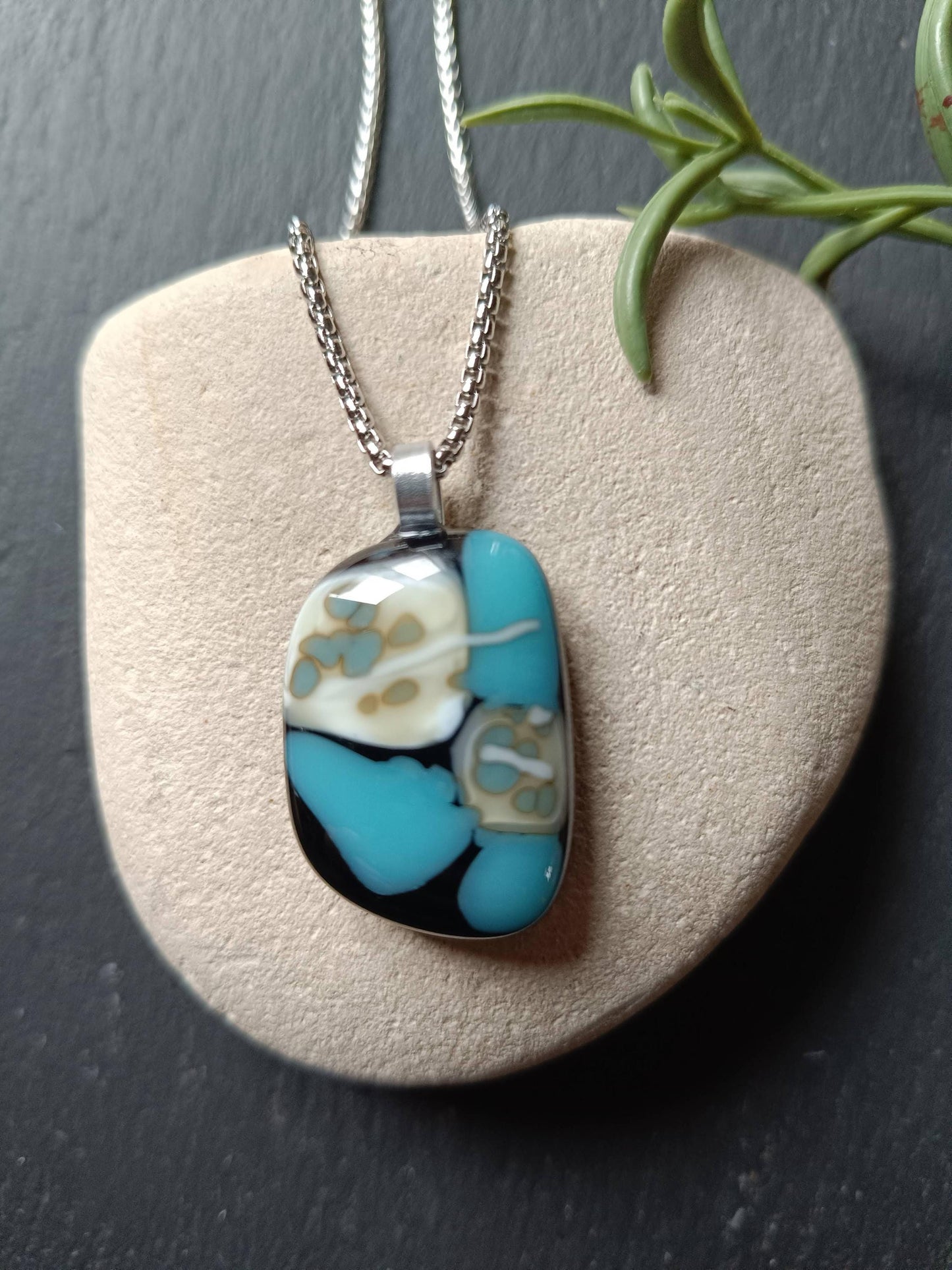 A silver coloured chain necklace with a turquoise, white, and black glass pendant.