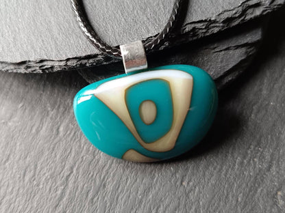 A teal blue glass pendant with white and gold abstract designs. The pendant is attached to a black cord.