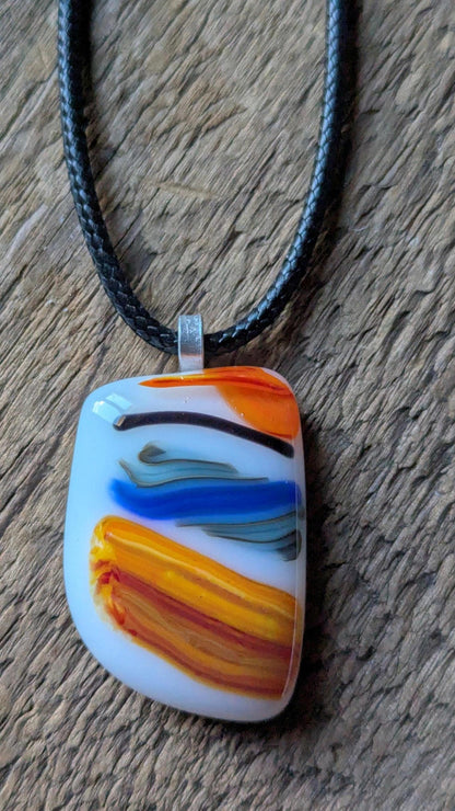 Large colorful fused glass pendant on black cord; white base with orange, yellow and blue swirls—handmade artisan jewellery.