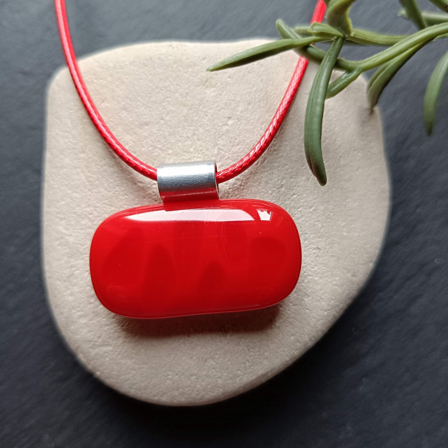 A red glass pendant on a red cord necklace. The pendant is oval shaped and has a silver bail.