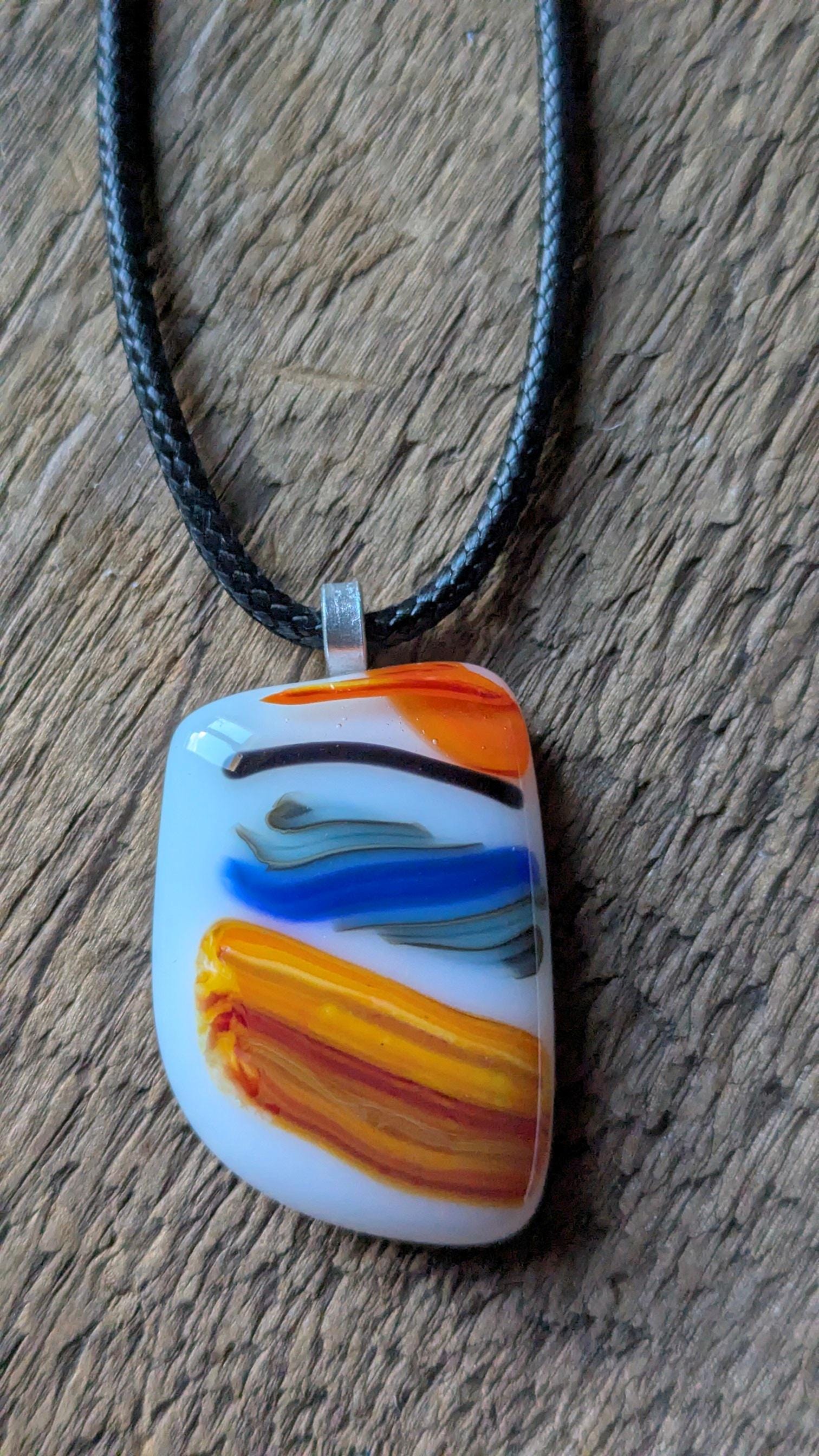 Large colorful fused glass pendant on black cord; white base with orange, yellow and blue swirls—handmade artisan jewellery.