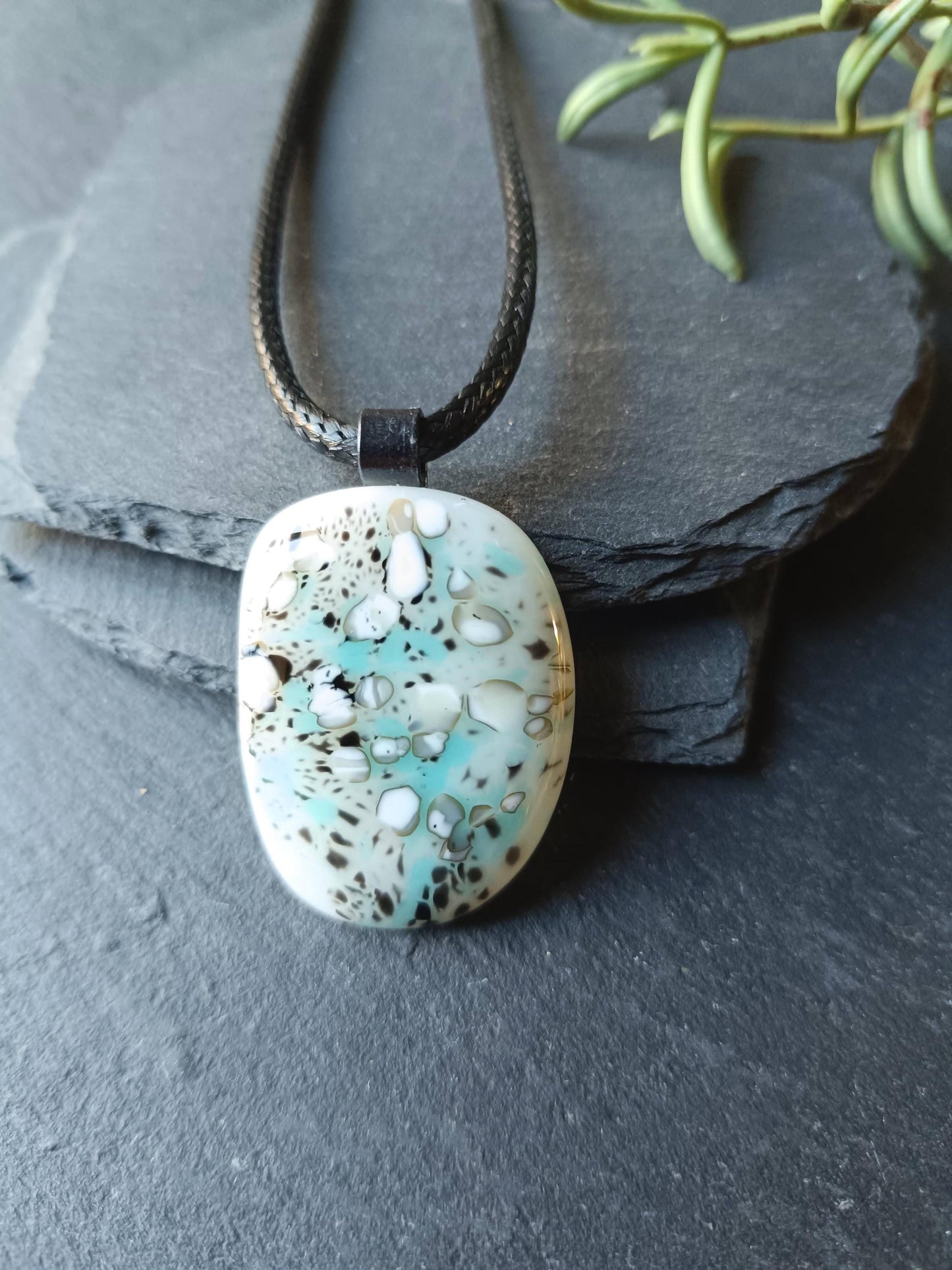 May include: A turquoise, white and black glass pendant on a black cord necklace. The pendant has a unique marbled pattern.