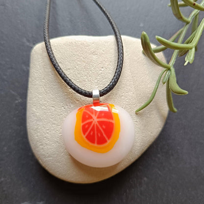 Fused glass orange pendant necklace on black cord; white round disc with bright orange slice, handmade one-of-a-kind jewelry.