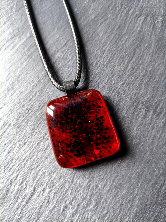 Red transparent fused glass pendant on a dark cord necklace; handmade necklace with black speckles.