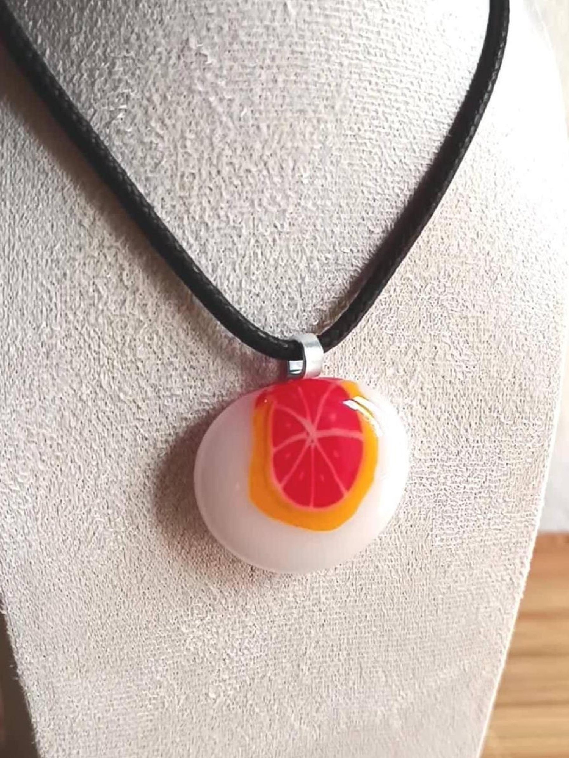 Fused glass orange pendant necklace on black cord; white round disc with bright orange slice, handmade one-of-a-kind jewelry.