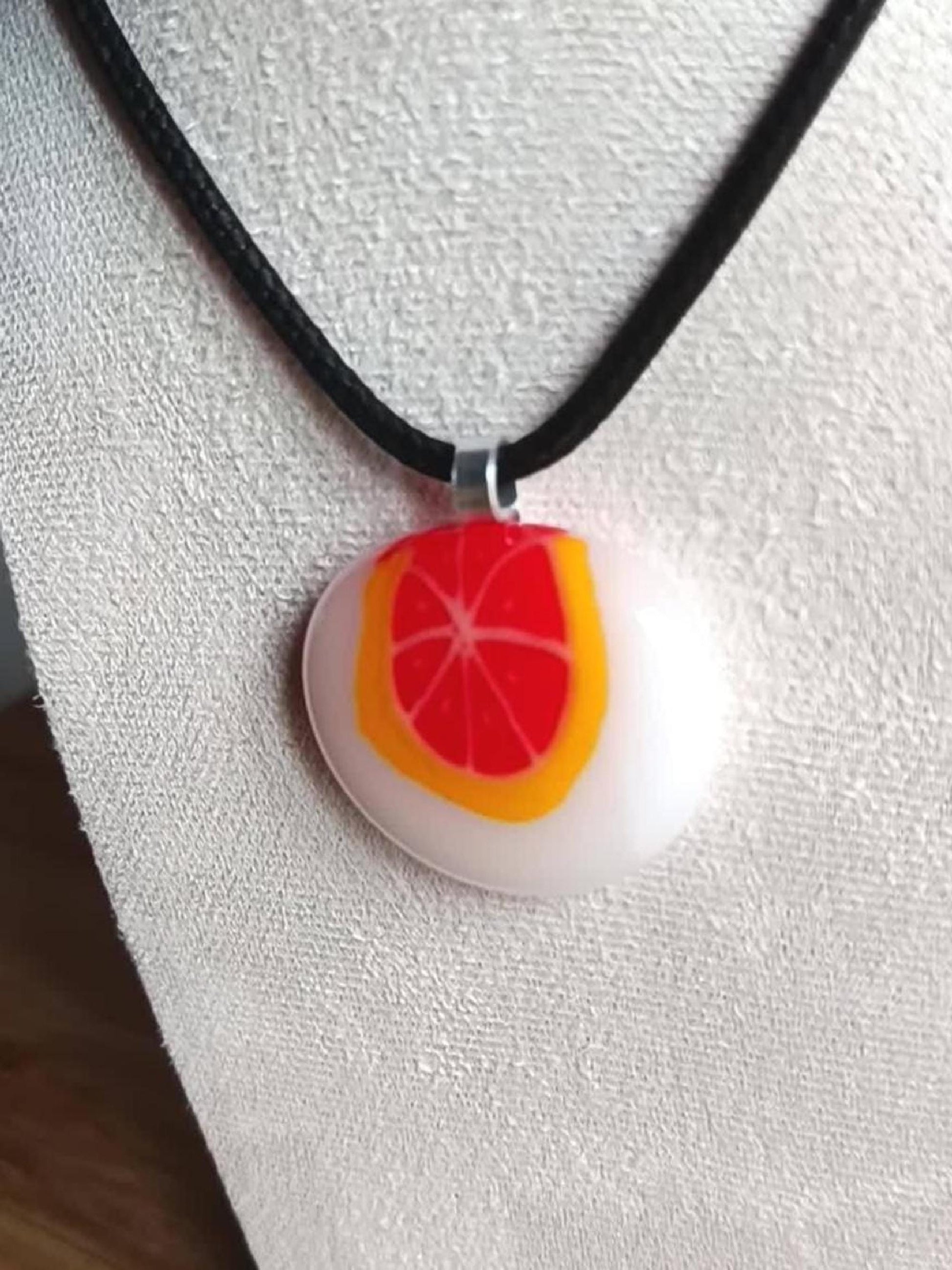 Fused glass orange pendant necklace on black cord; white round disc with bright orange slice, handmade one-of-a-kind jewelry.
