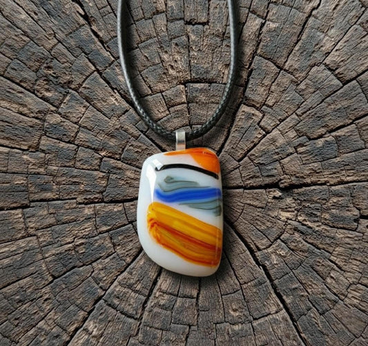 Large colorful fused glass pendant on black cord; white base with orange, yellow and blue swirls—handmade artisan jewellery.