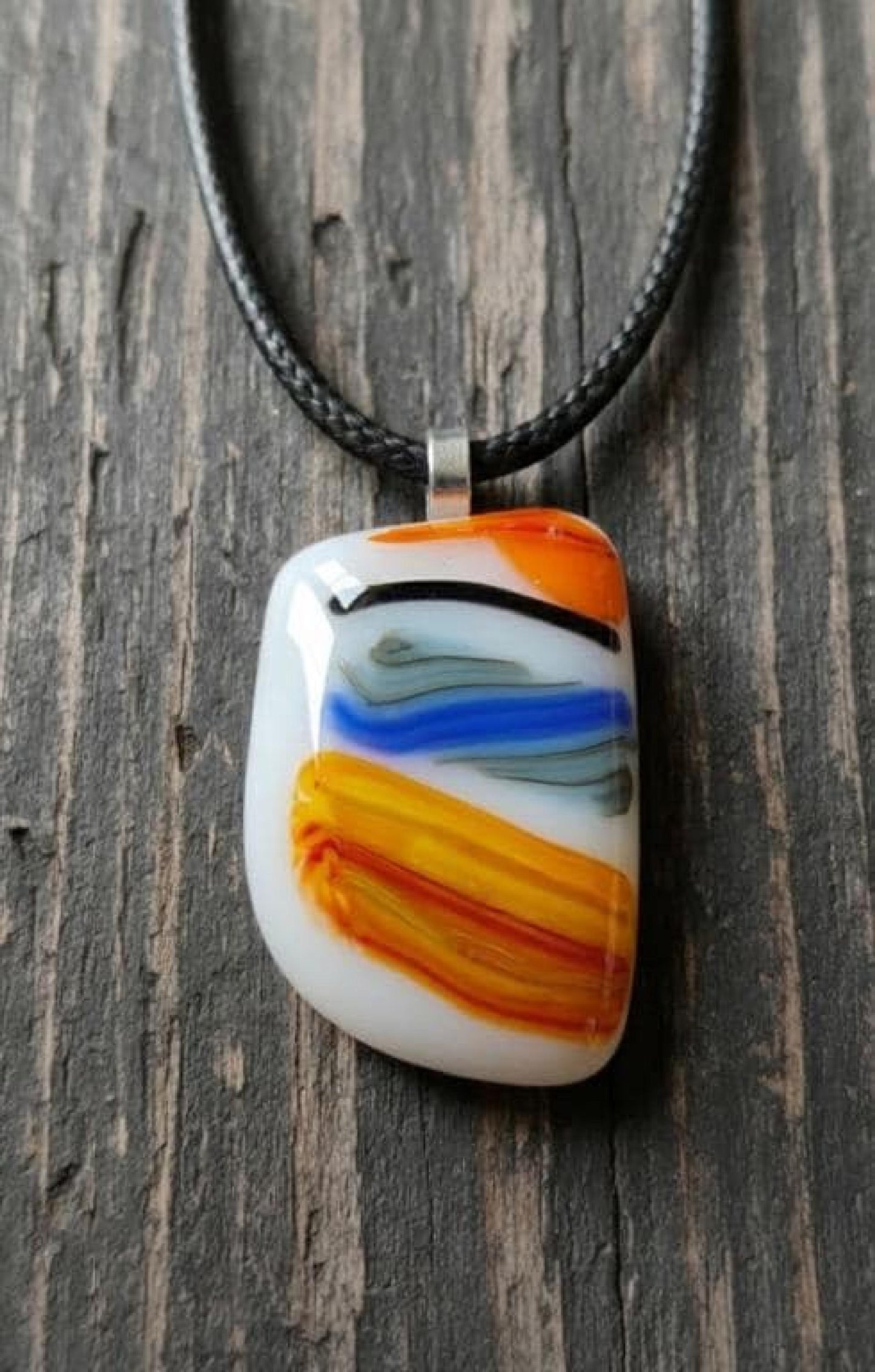 Large colorful fused glass pendant on black cord; white base with orange, yellow and blue swirls—handmade artisan jewellery.