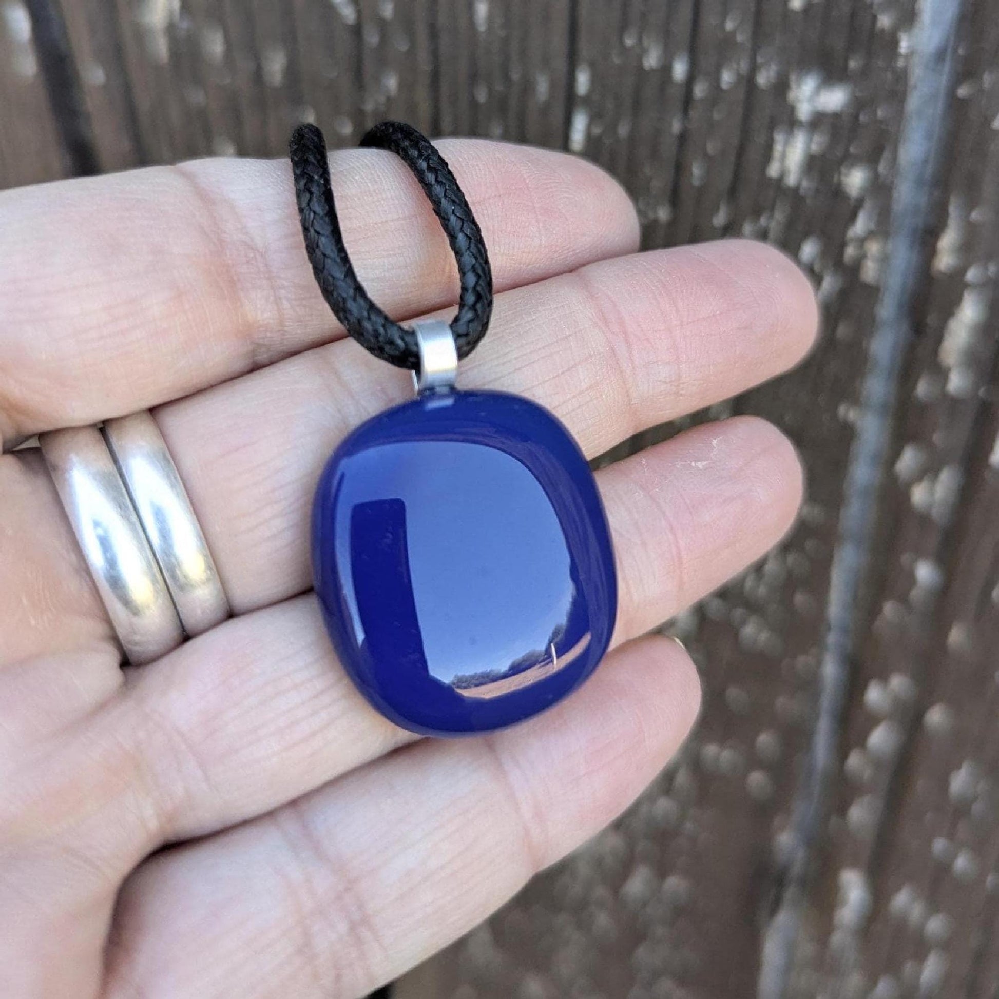 Blue fused glass pendant on a black cord necklace; smooth cobalt-blue oval pendant, handmade artisan jewelry.