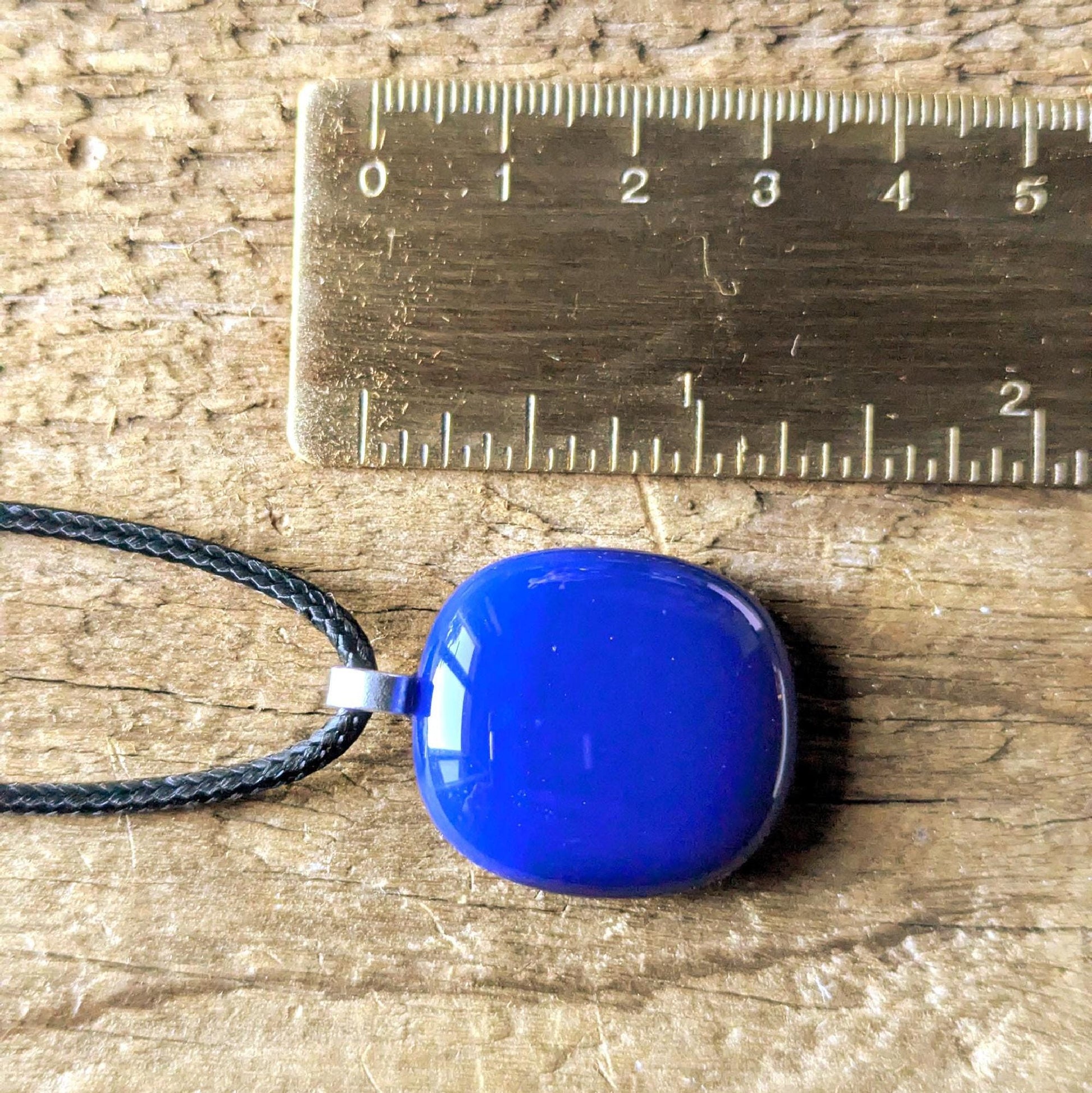 Blue fused glass pendant on a black cord necklace; smooth cobalt-blue oval pendant, handmade artisan jewelry.