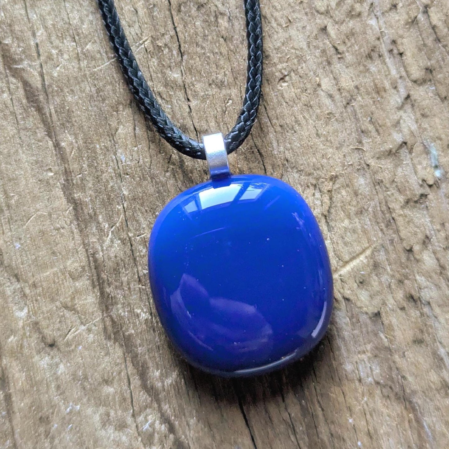 Blue fused glass pendant on a black cord necklace; smooth cobalt-blue oval pendant, handmade artisan jewelry.