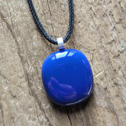 Blue fused glass pendant on a black cord necklace; smooth cobalt-blue oval pendant, handmade artisan jewelry.
