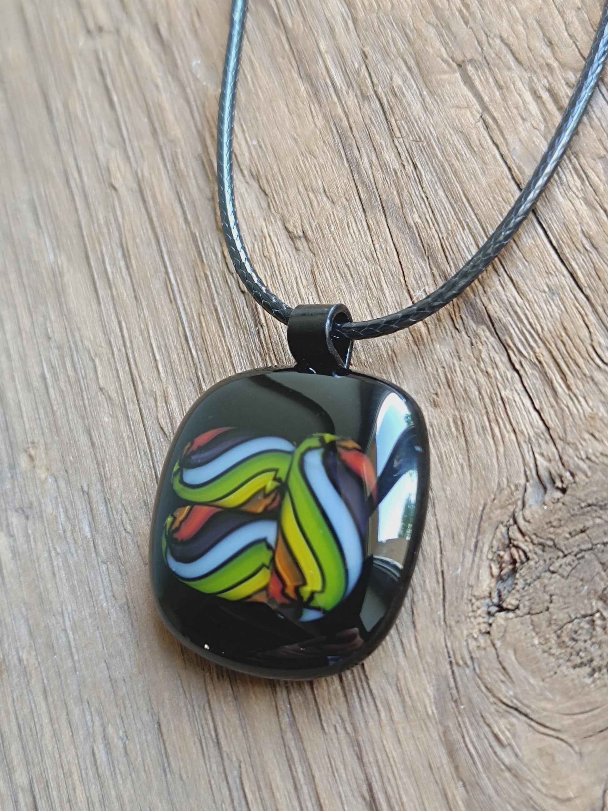 Square glass pendant in black bezel with multicolor swirl in green, blue, yellow, red on a black cord necklace.