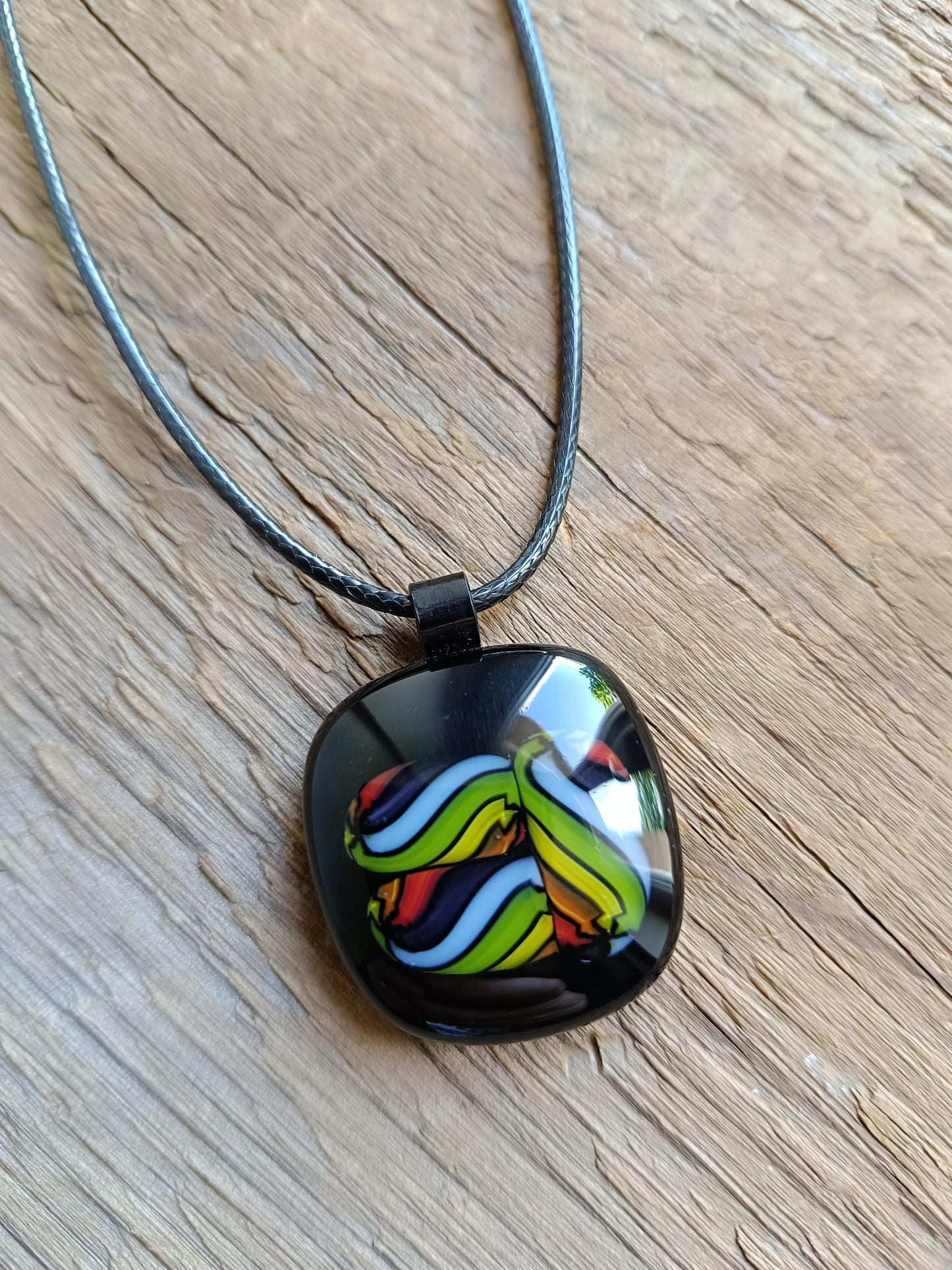 Square glass pendant in black bezel with multicolor swirl in green, blue, yellow, red on a black cord necklace.