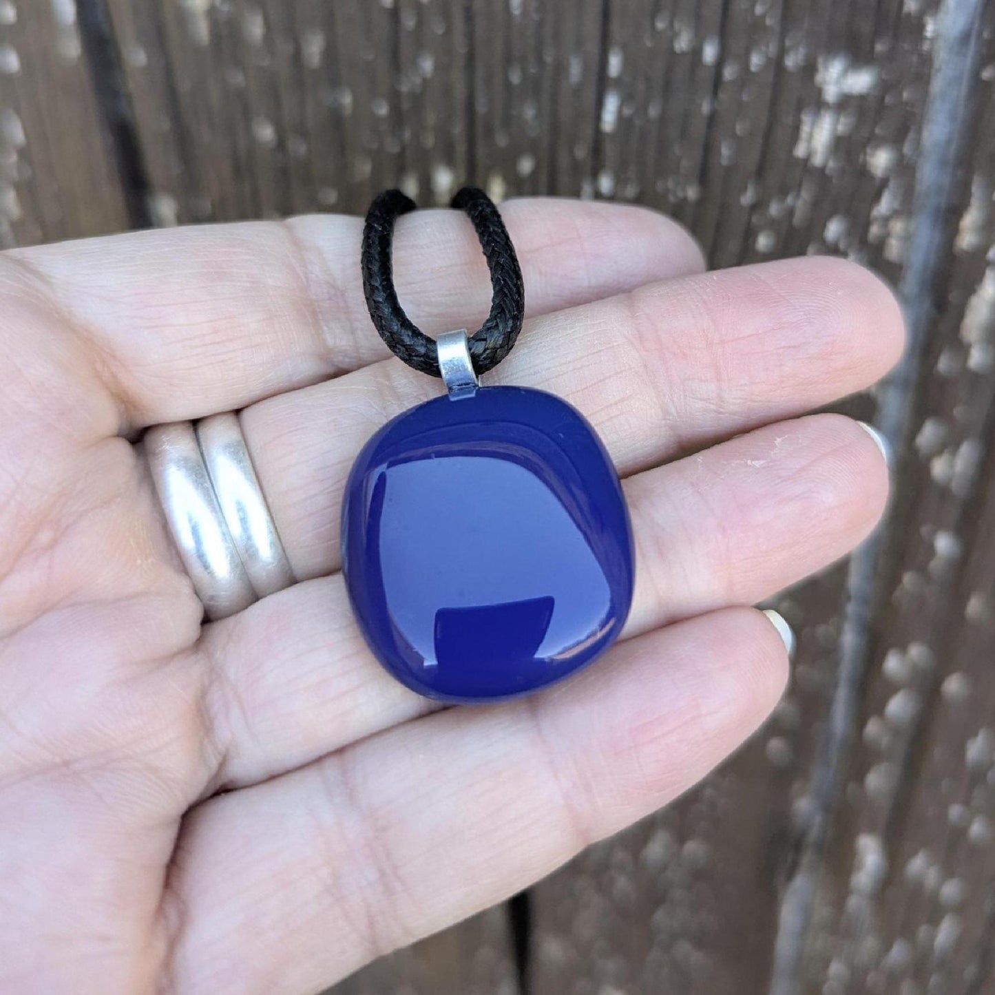 Blue fused glass pendant on a black cord necklace; smooth cobalt-blue oval pendant, handmade artisan jewelry.