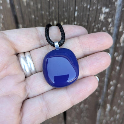 Blue fused glass pendant on a black cord necklace; smooth cobalt-blue oval pendant, handmade artisan jewelry.