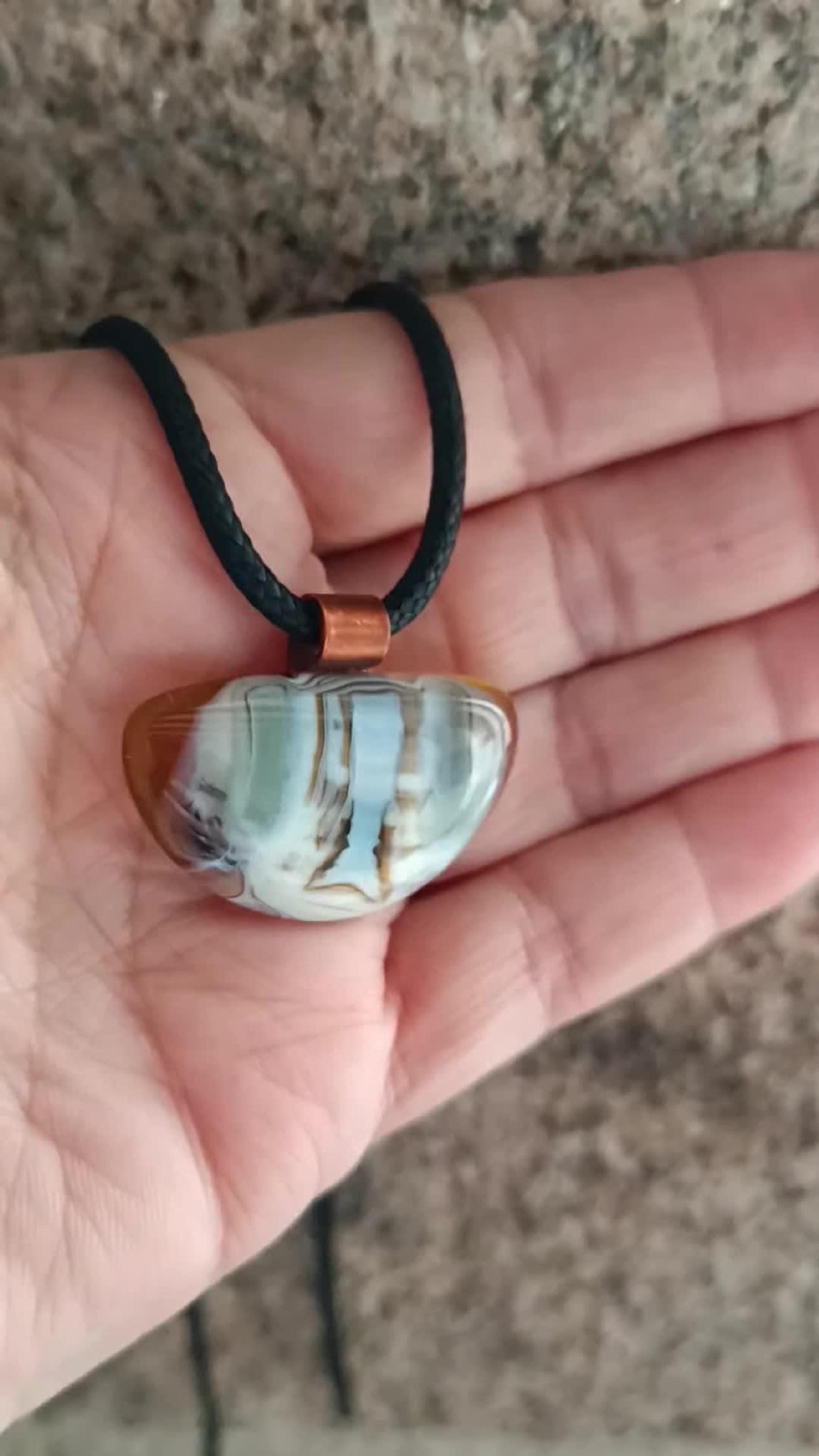 Fused glass pendant on a grunge black cord necklace with copper bail; orange bottom with blue-green swirls and brown lines.