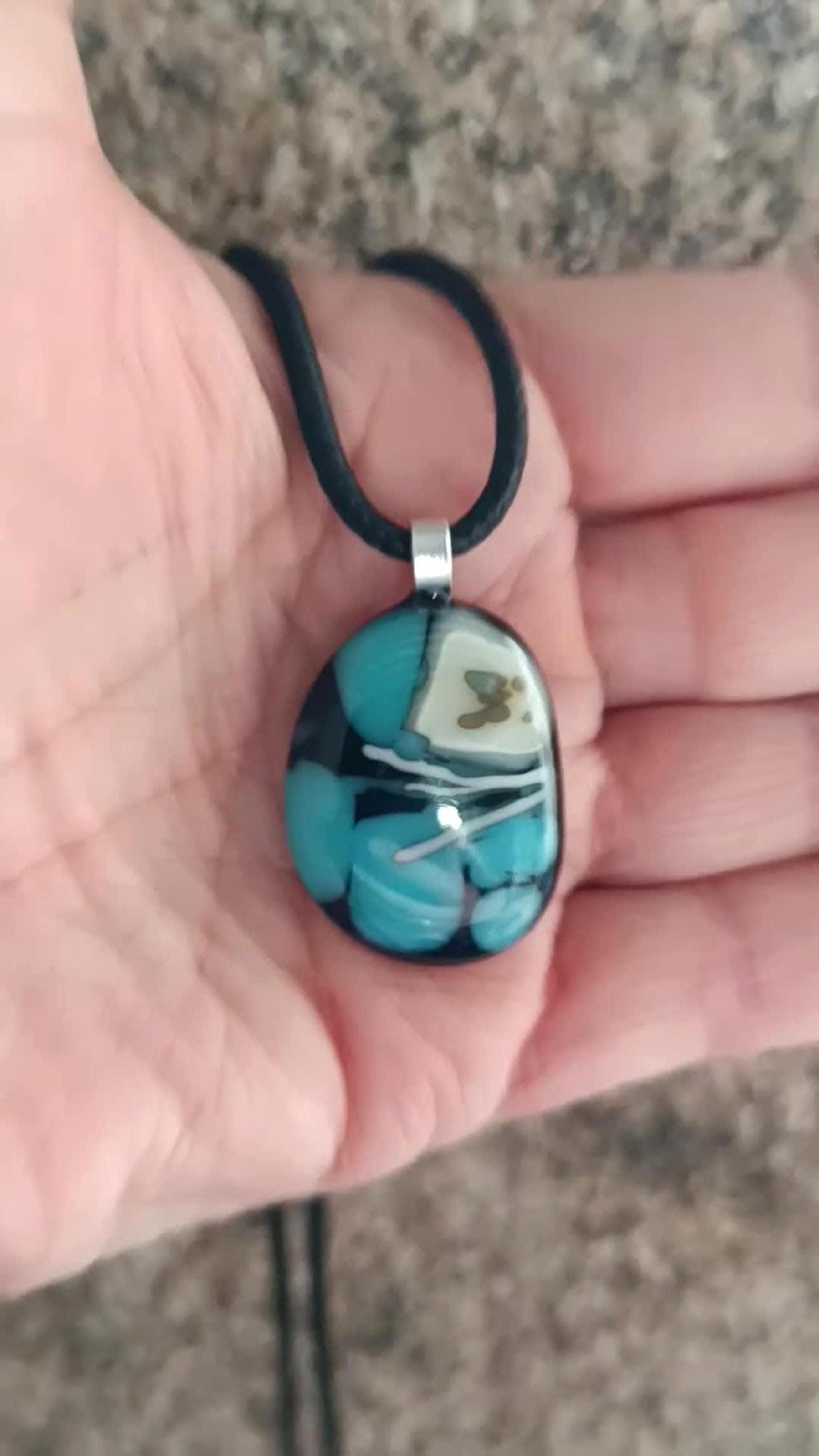 Fused glass pendant necklace in blue and black tones with white swirls and a silver bail on a black cord.