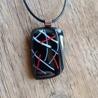 Fused glass pendant on black cord necklace with abstract white, blue, red lines; quirky art pendant, handmade jewellery.